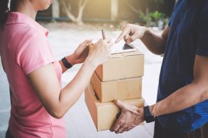 Woman customer appending signature in digital tablet and receiving a cardboard boxes parcel from